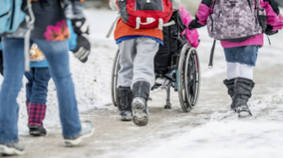 Kind im Rollstuhl wird durch Schnee geschoben
